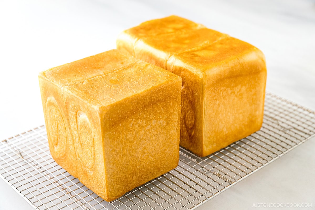 Two loaves of Japanese milk bread (flat-topped and round-topped) on a wire rack.