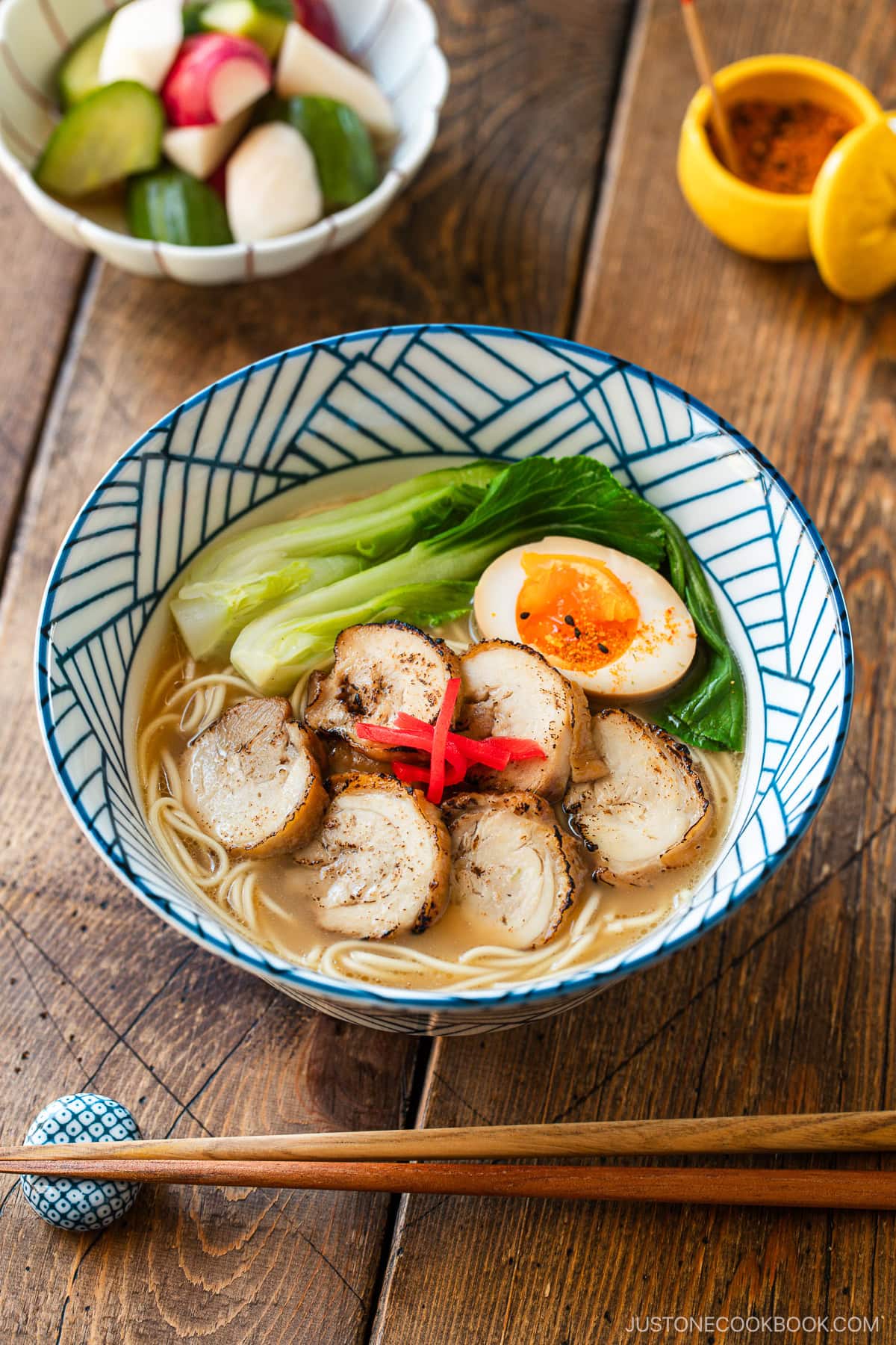 Blue and white bowls containing ramen with soup topped with seared sliced chicken chashu, soft boiled egg, and blanched bok choy, and garnished with pickled ginger.