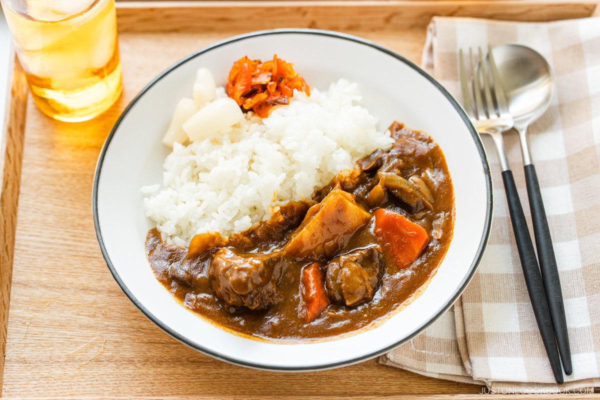 A round white plate containing Japanese beef curry consisting of tender beef, potatoes, carrots, mushrooms, and curry roux, served over steamed rice.