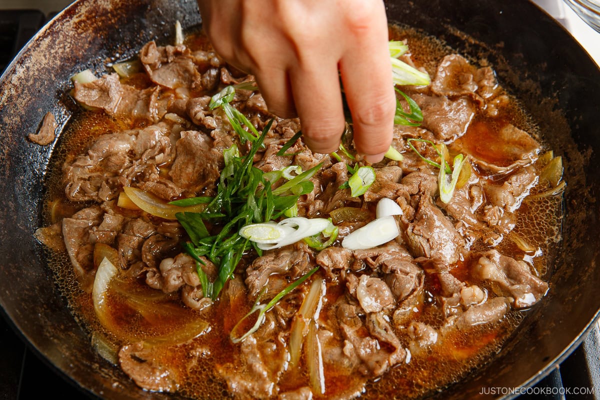 Add thinly sliced green onions on the simmering beef.