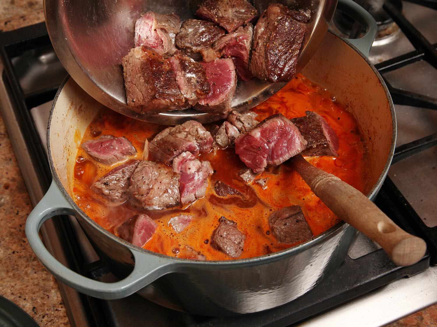 Adding cut pieces of seared beef into the stew liquid for goulash. 