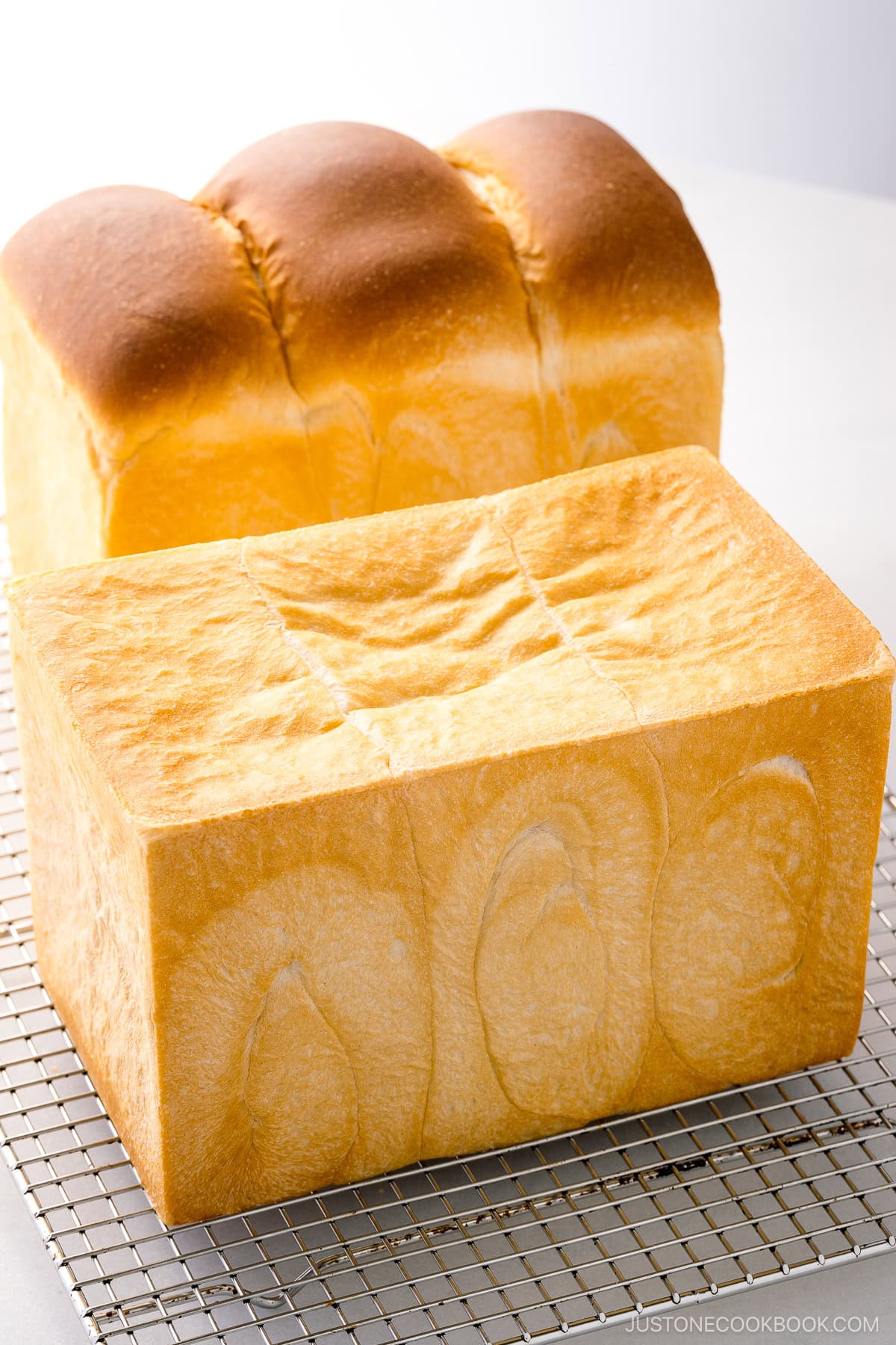 Two loaves of Japanese milk bread (shokupan), one with round topped and the other with flat topped, placed on a wire rack.