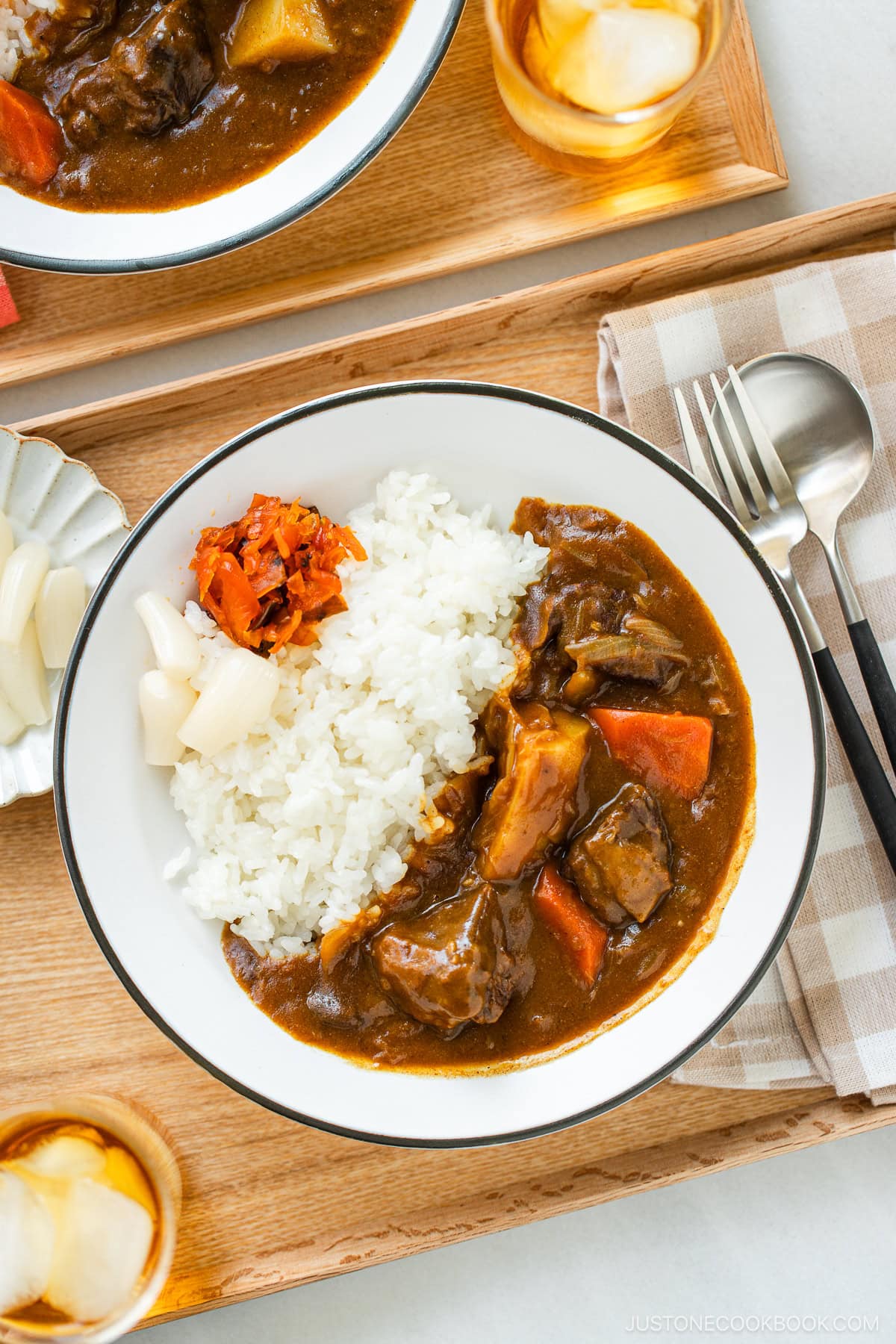 A round white plate containing Japanese beef curry consisting of tender beef, potatoes, carrots, mushrooms, and curry roux, served over steamed rice.