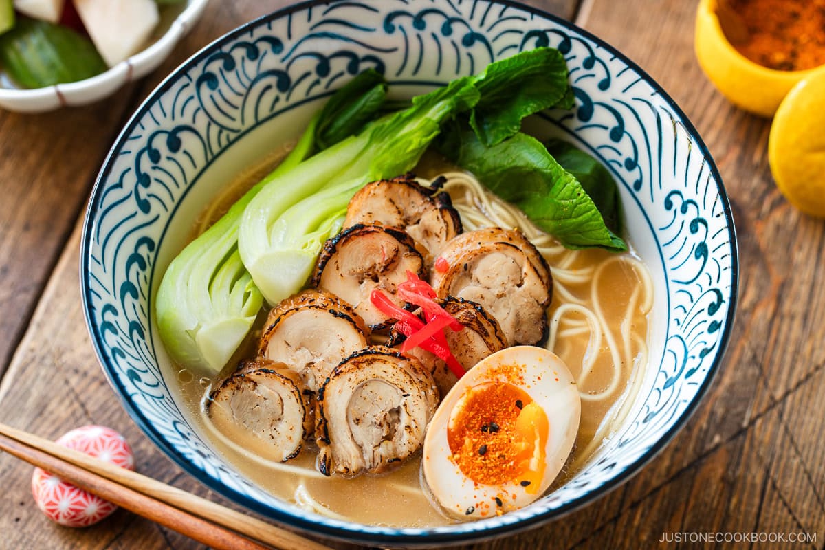 Blue and white bowls containing ramen with soup topped with seared sliced chicken chashu, soft boiled egg, and blanched bok choy, and garnished with pickled ginger.