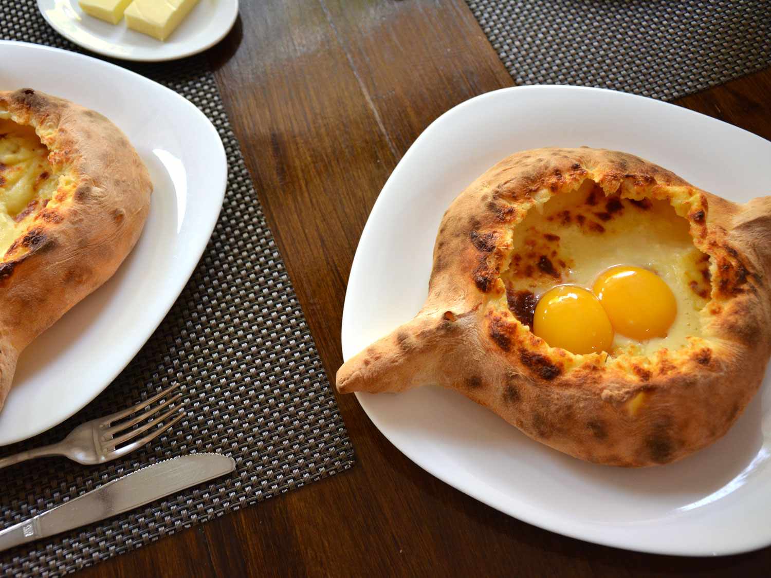 Khachapuri adjaruli resting on a plate with two eggs on top. 