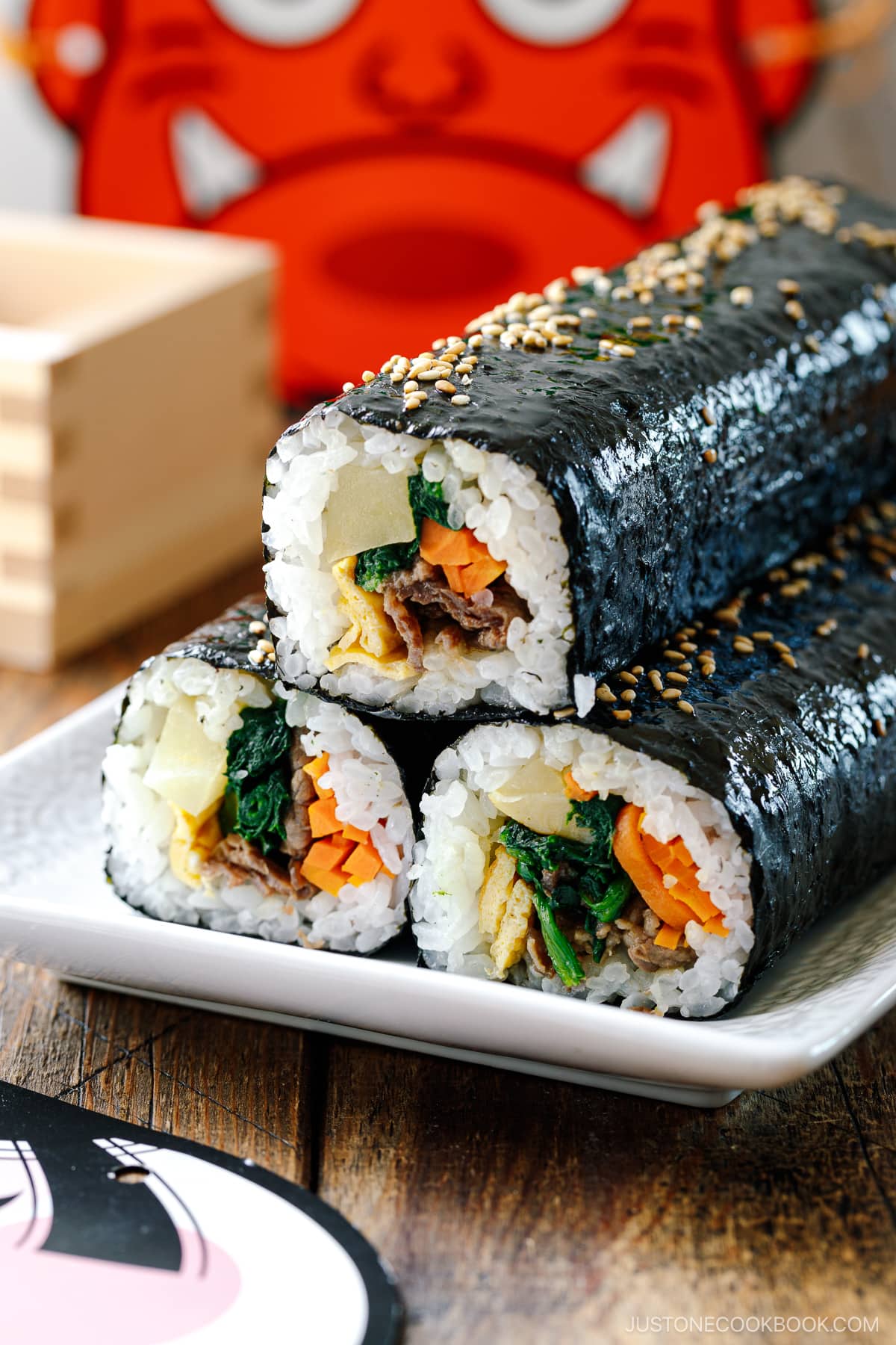 A rectangular plate containing three uncut rolls of Kimbap (Korean Seaweed Roll).