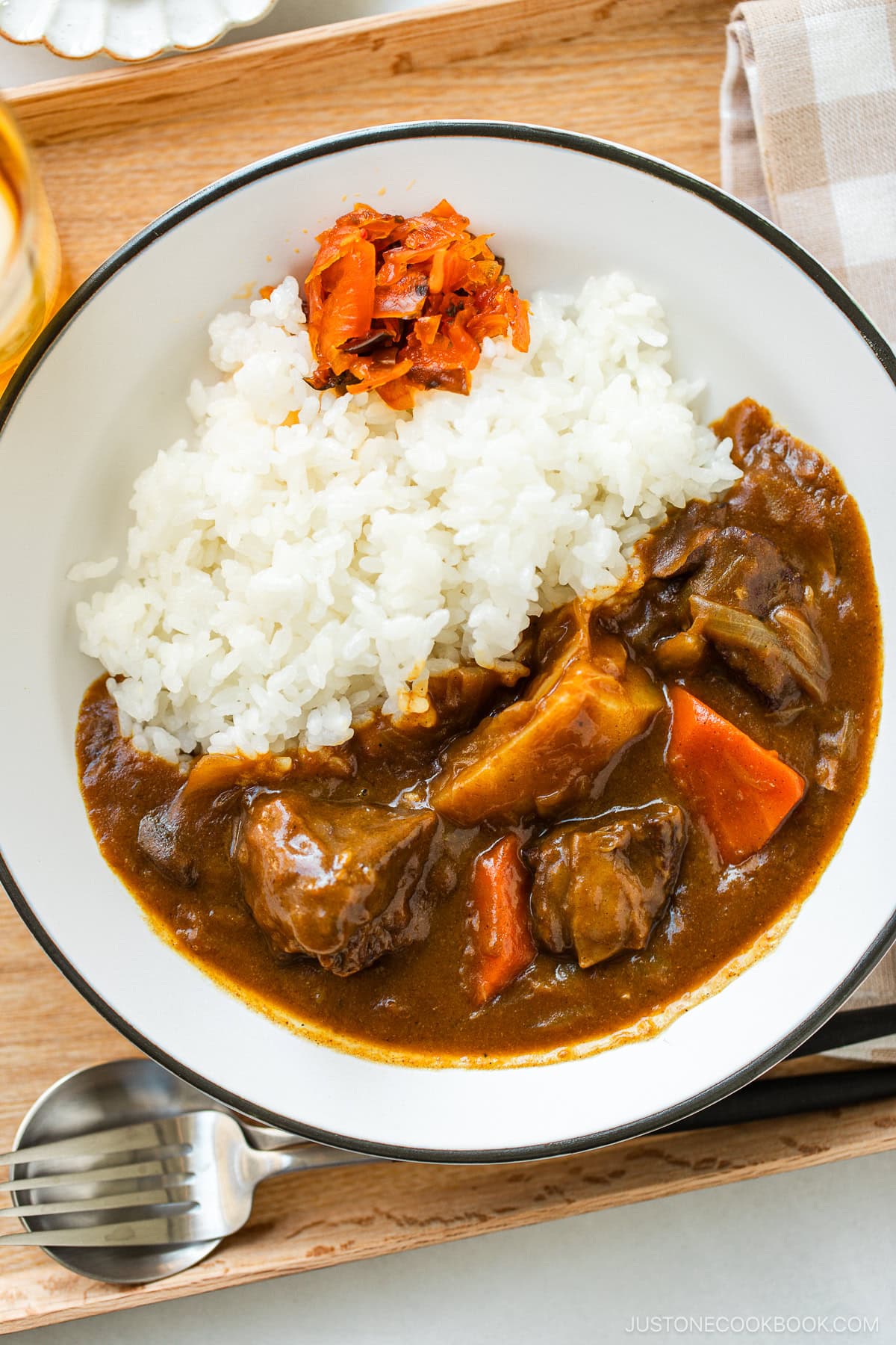 A round white plate containing Japanese beef curry consisting of tender beef, potatoes, carrots, mushrooms, and curry roux, served over steamed rice.