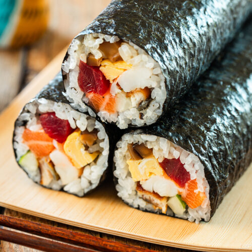 A rectangular plate containing three ehomaki, or uncut sushi rolls, prepared for setsubun festival.