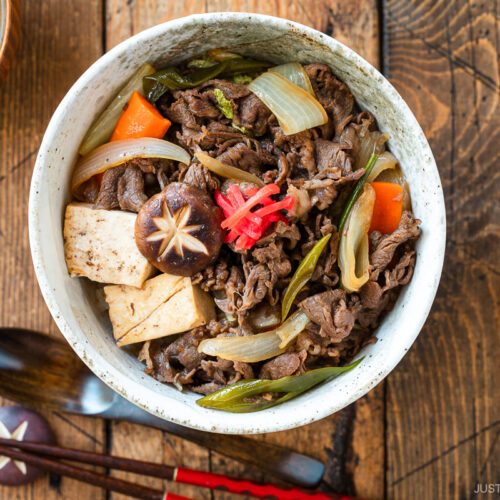 A large ceramic donburi rice bowl containing Sukiyaki Don, thinly sliced beef, tofu, and vegetables simmered in a savory dashi soy broth and served over steamed rice.