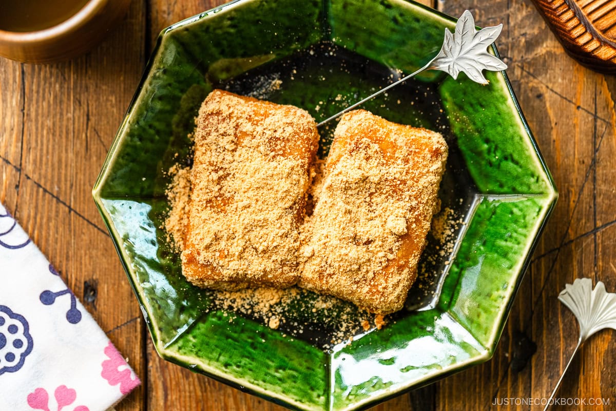 A green plate containing Japanese rice cake (mochi) coated with kinako (soybean flour).