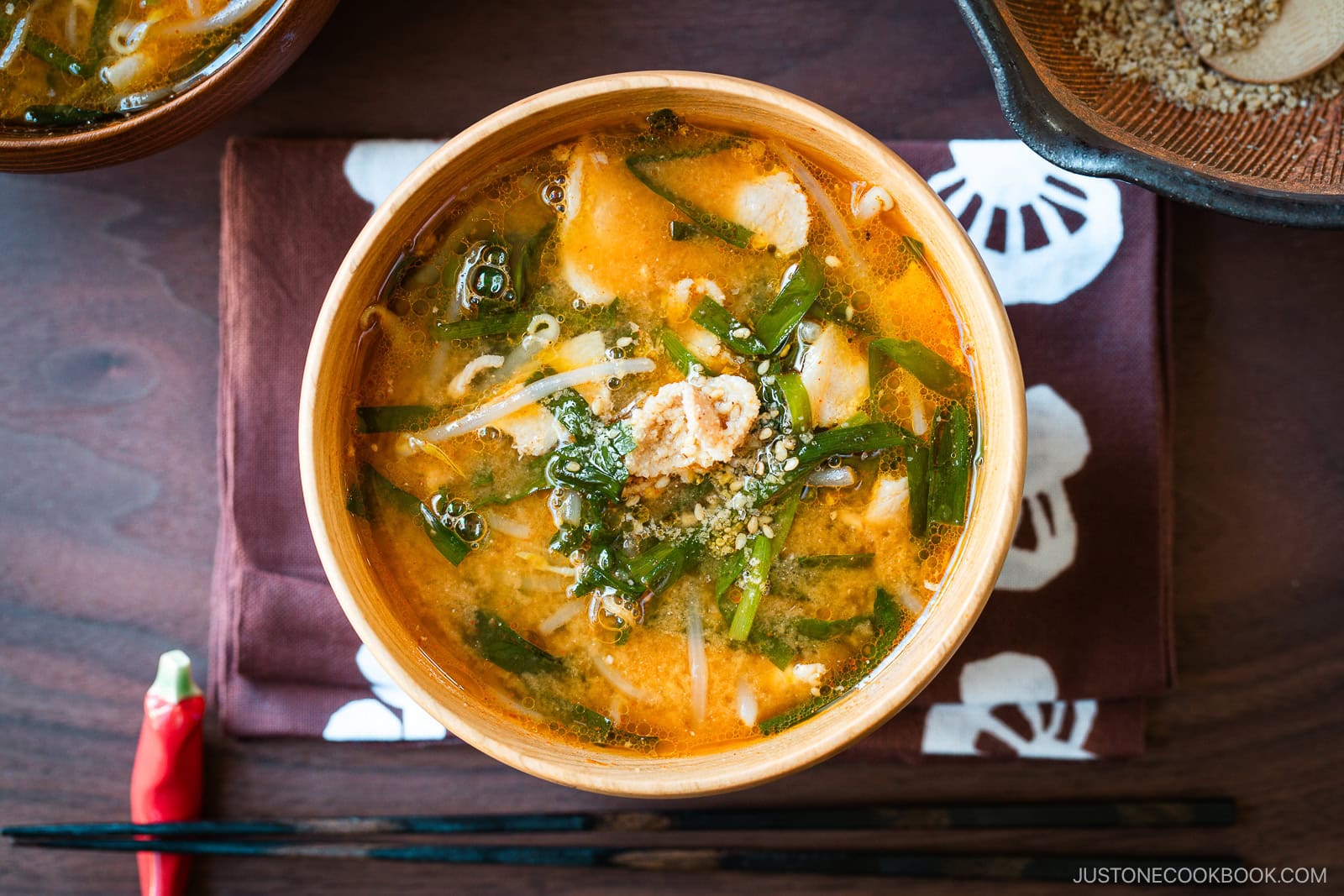 A light wooden bowl containing Spicy Pork and Bean Sprout Miso Soup sprinkled with ground sesame seeds.