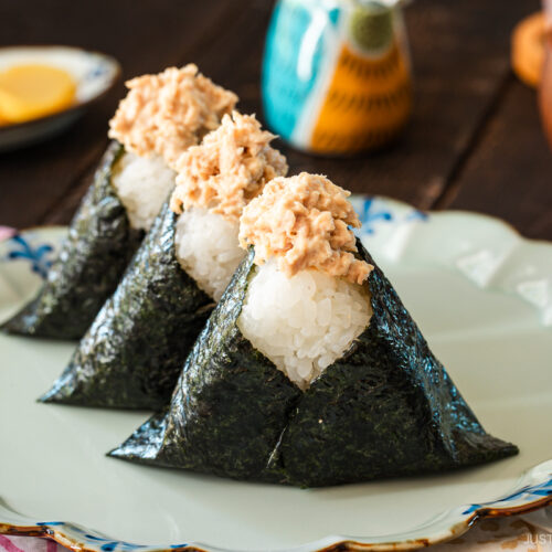 A plate containing three tuna mayo onigiri served with a wooden bowl of miso soup, a cup of tea, and a small dish of pickles.