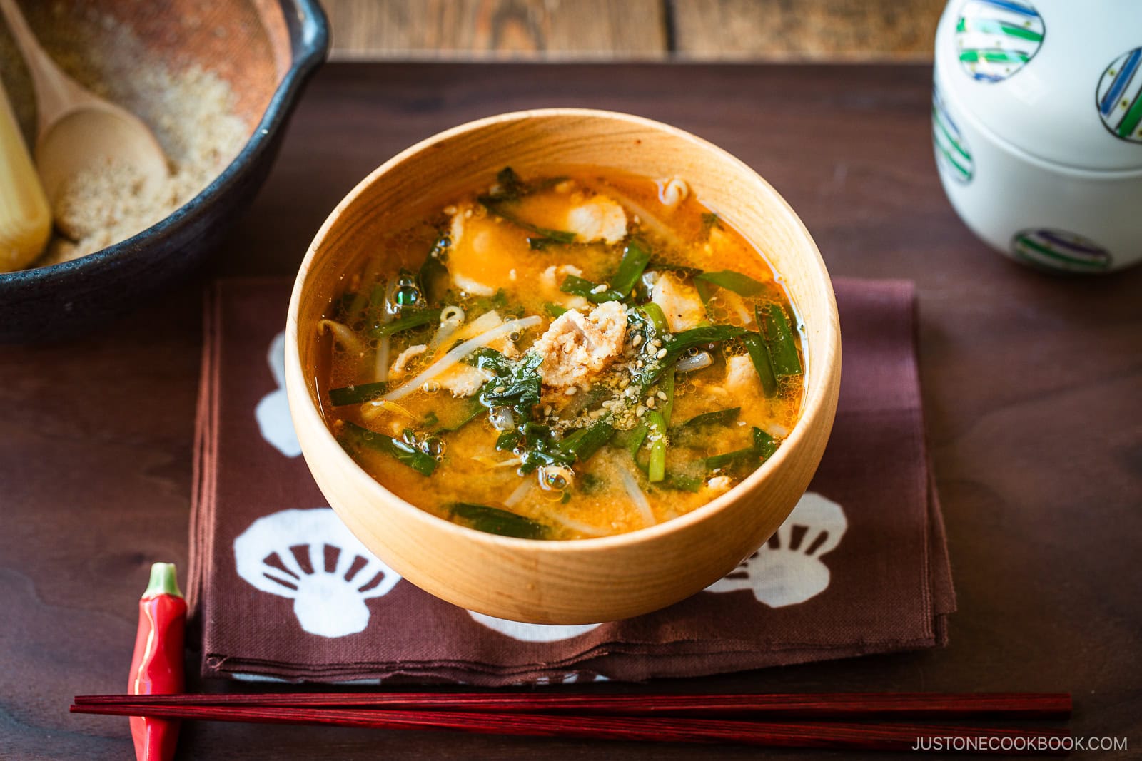 A light wooden bowl containing Spicy Pork and Bean Sprout Miso Soup sprinkled with ground sesame seeds.