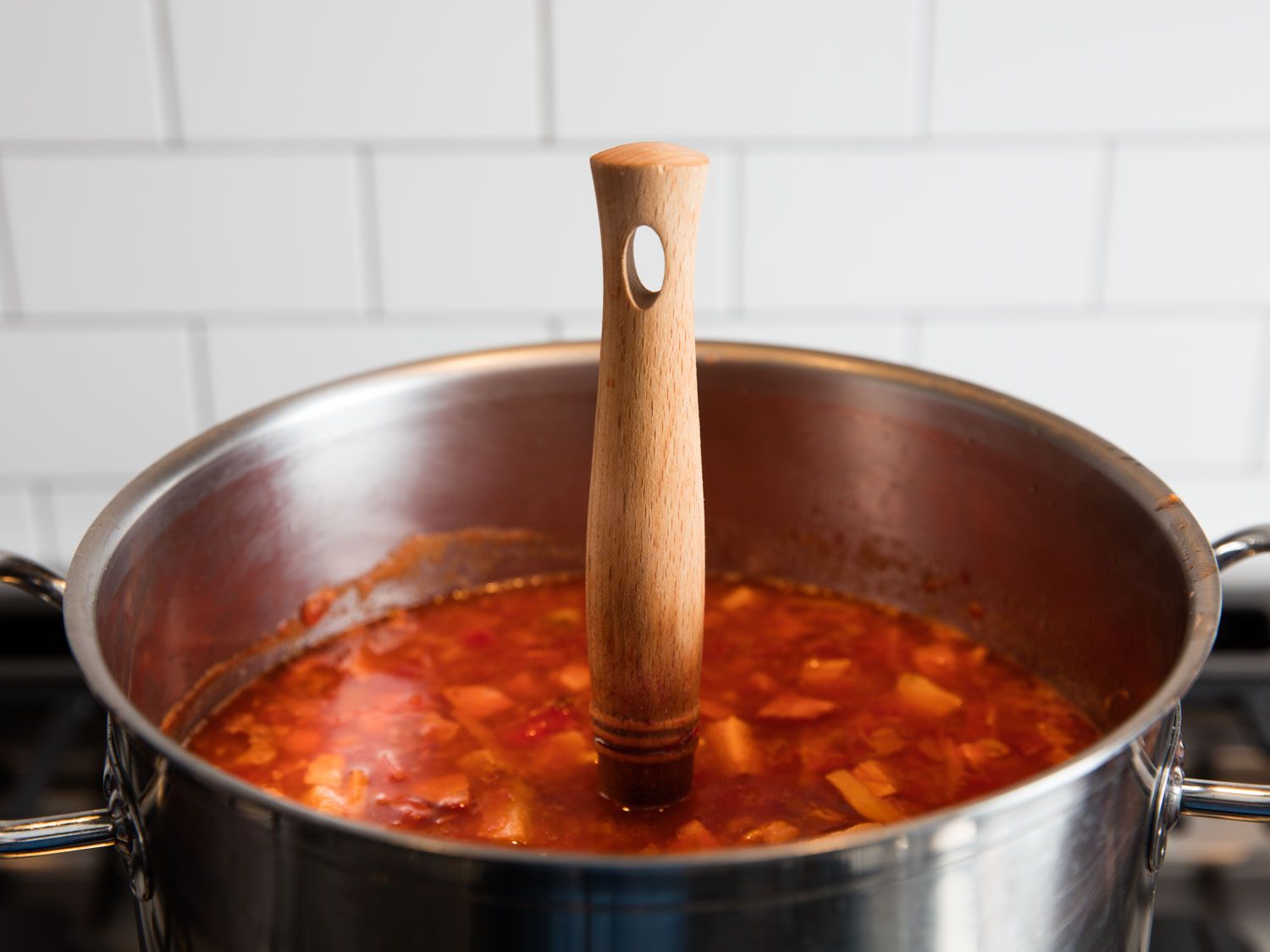 Wooden spoon standing on end in the middle of a pot full of thick borscht.