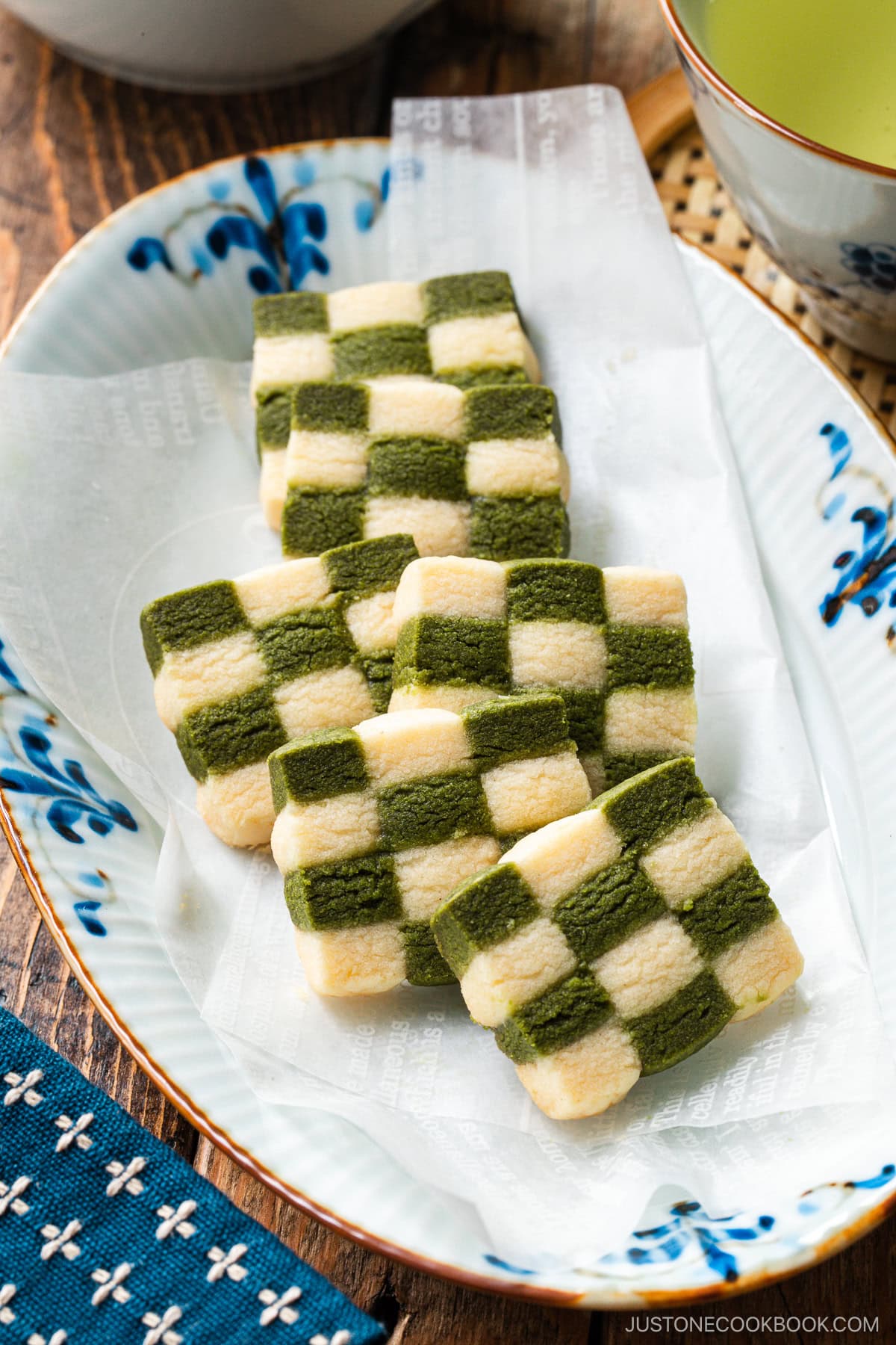 An oval plate containing Matcha Checkerboard Cookies served with a cup of green tea.