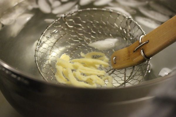 Author scooping up cooked and cooled spätzle out of an ice bath.