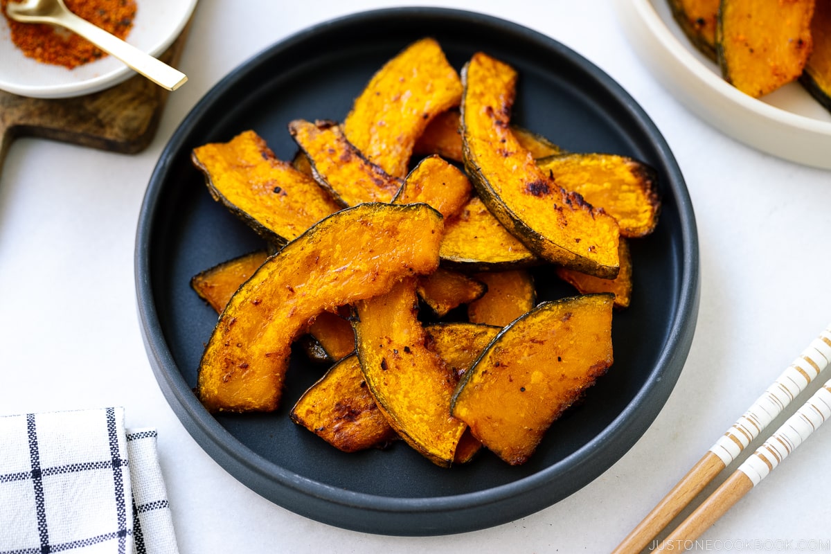 A black round ceramic plate containing roasted kabocha slices.