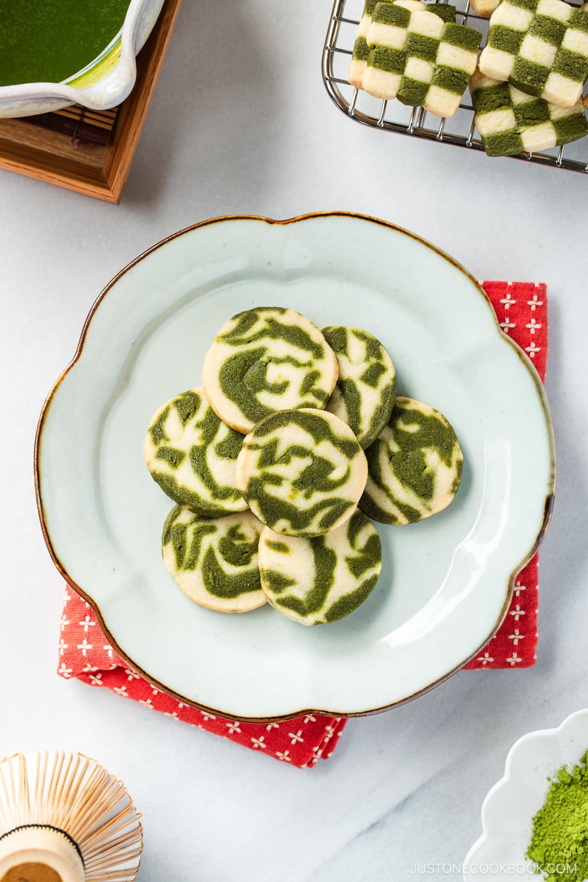 A plate containing Matcha Checkerboard Cookies served with a cup of matcha and bamboo whisk.