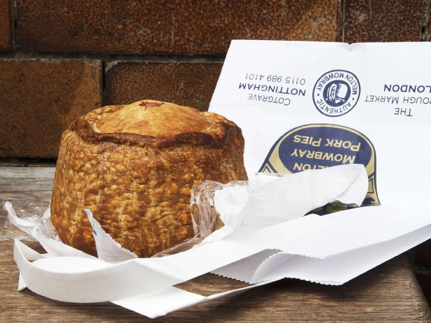 A whole Melton Mowbray pork pie, unwrapped, next to a paper shopping bag from Mrs. King's.