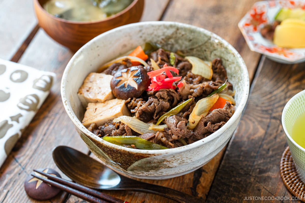 A large ceramic donburi rice bowl containing Sukiyaki Don, thinly sliced beef, tofu, and vegetables simmered in a savory dashi soy broth and served over steamed rice.