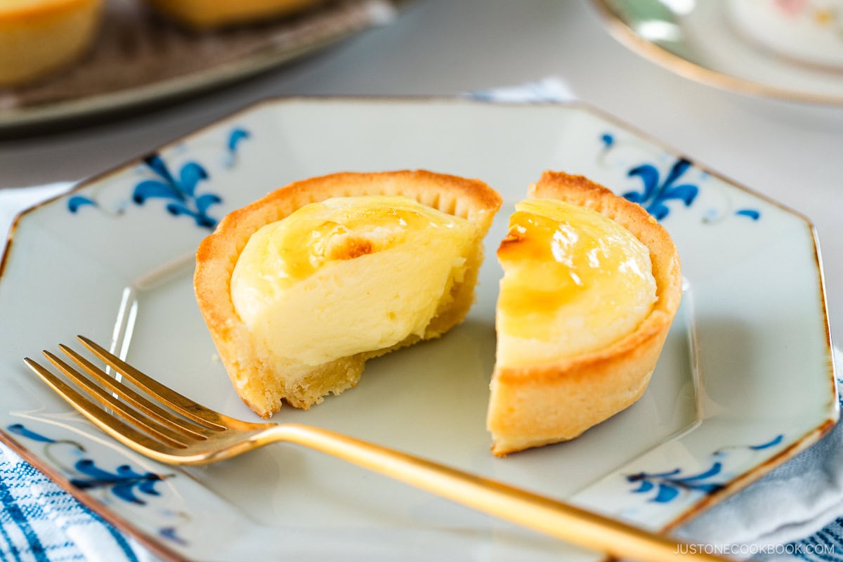 An octagon plate containing baked cheese tart, cut in half, creamy, soft cheese melting and oozing out from the crispy crust.