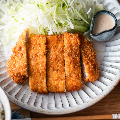 A Japanese ceramic plate containing Tonkatsu (pork cutlet) and shredded cabbage salad.