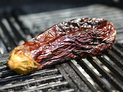 Eggplant being roasted on a grill, its skin shriveling and charred. 