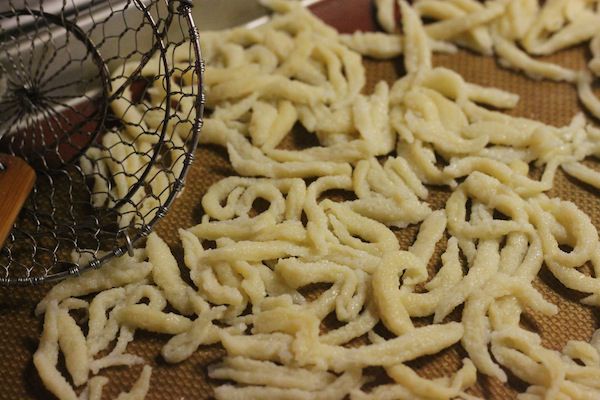 Cooked and cooled spätzle are transferred to a rimmed baking sheet to dry.