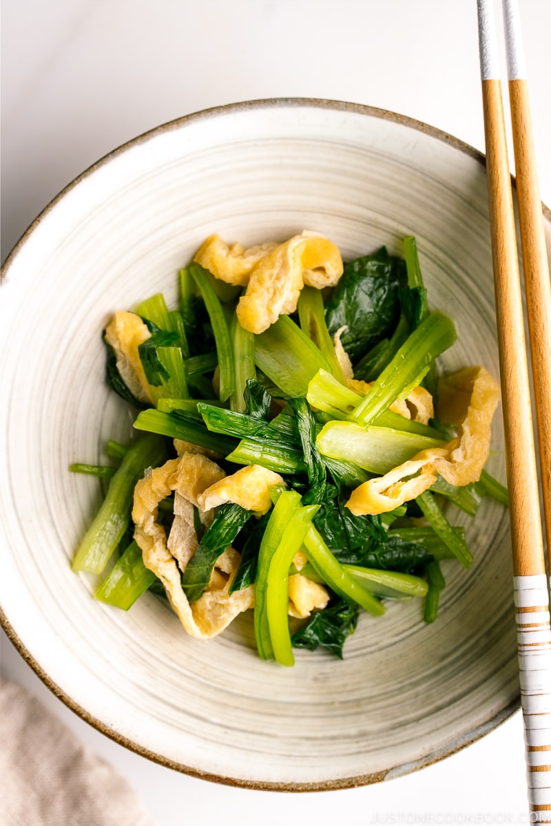 A white Japanese ceramic bowl containing Simmered Fried Tofu and Greens.