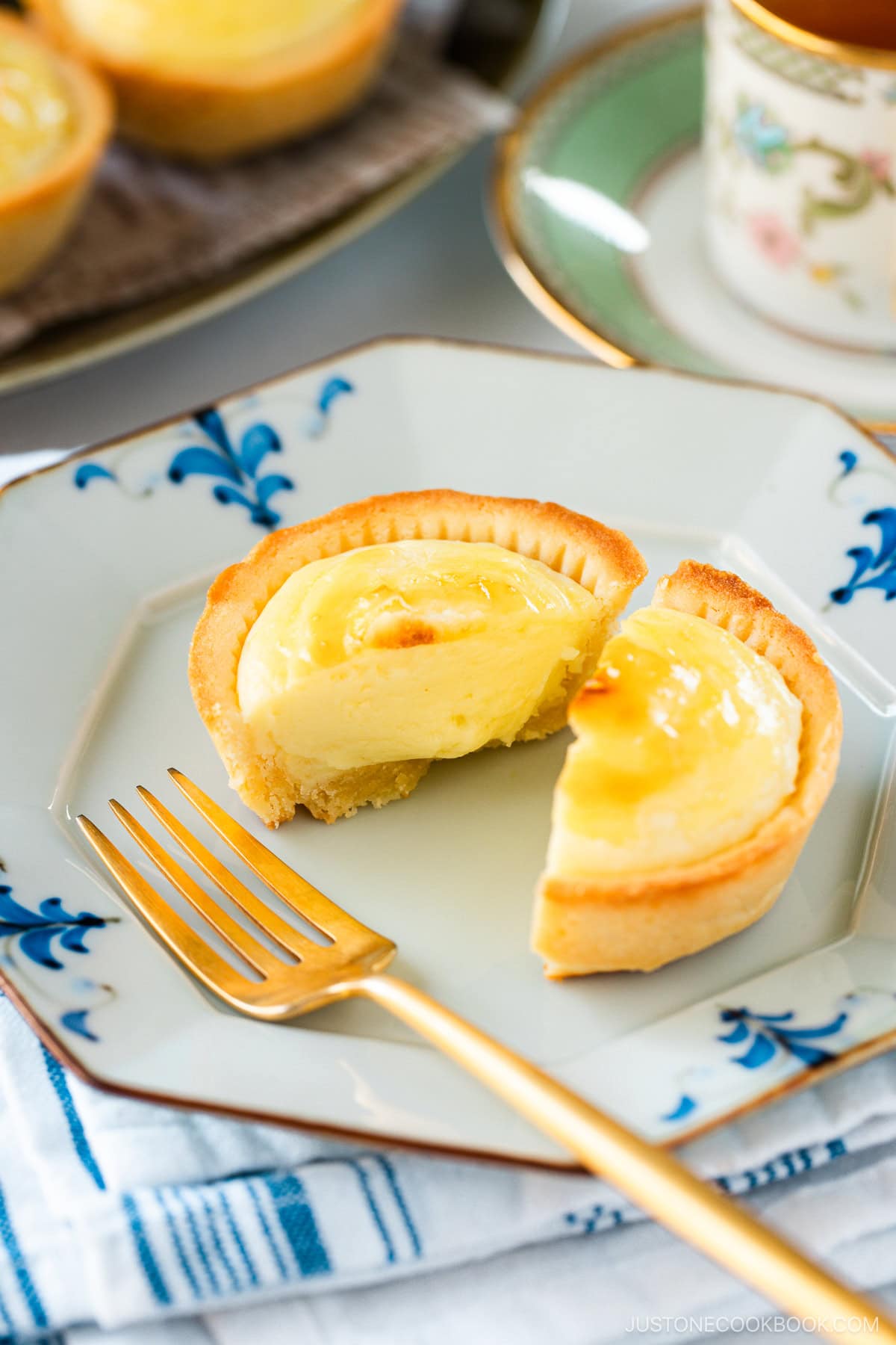 An olive oval plate and a white flower-shaped plate containing baked cheese tarts, served with a cup of tea.