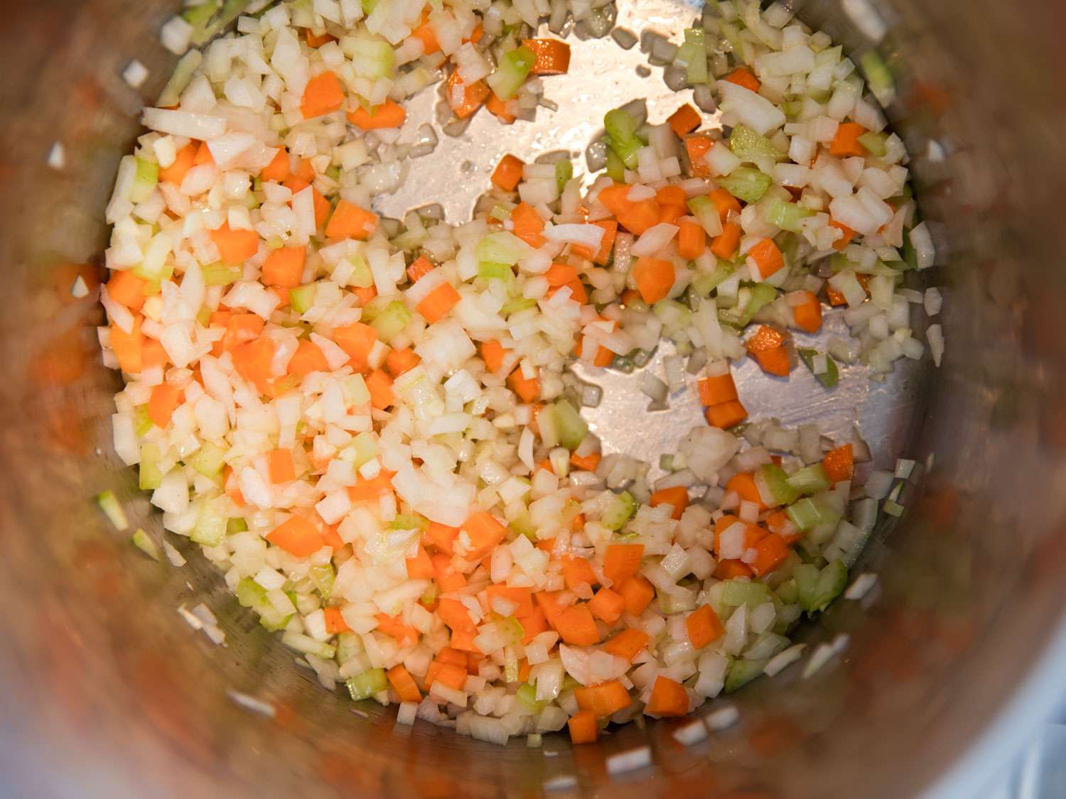 Overhead shot of diced onions, celery, and carrots in the bottom of a stockpot. 