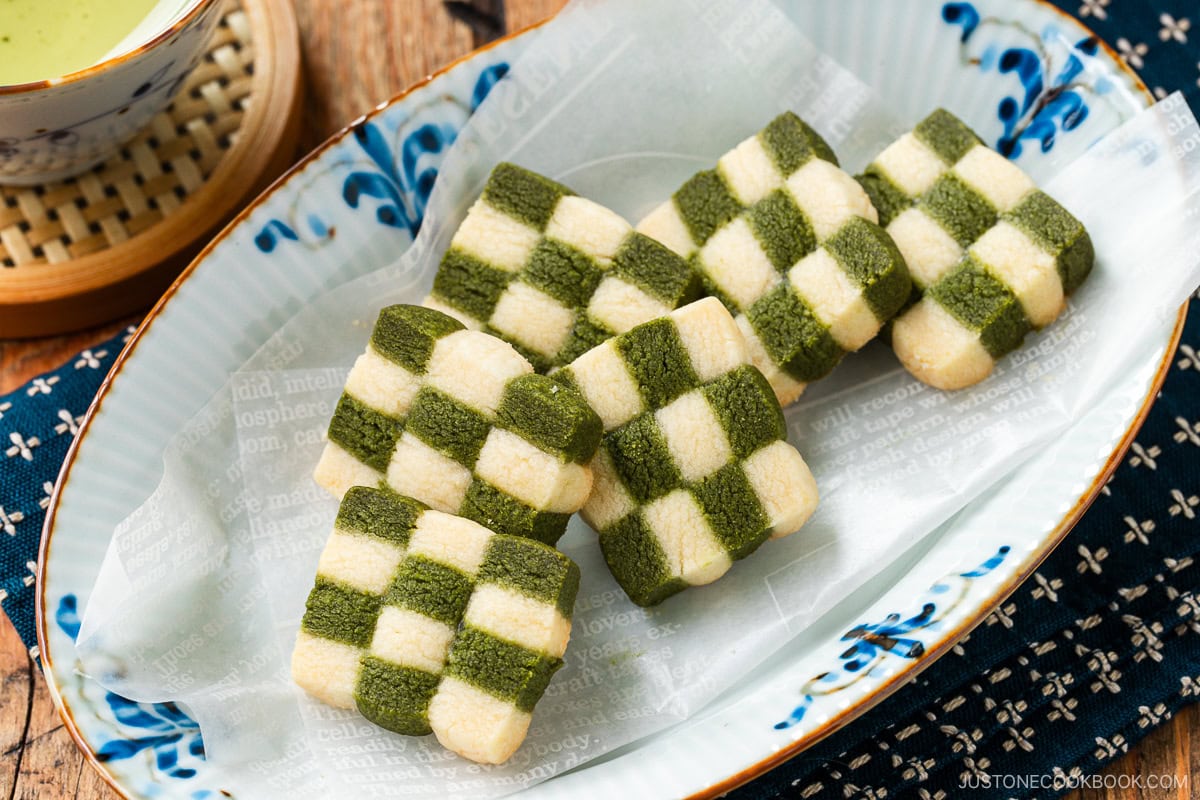 An oval plate containing Matcha Checkerboard Cookies served with a cup of green tea.