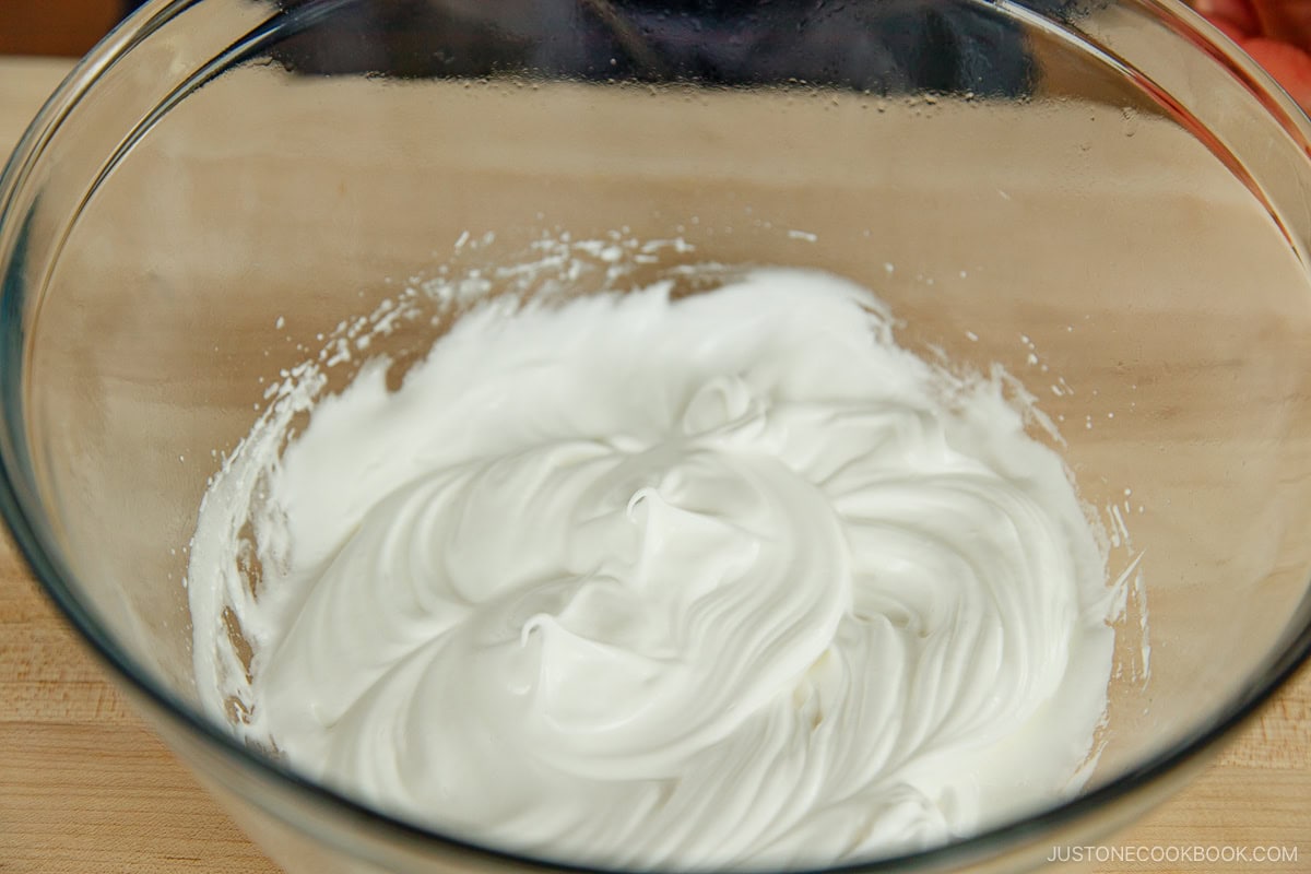 A glass mixing bowl containing egg whites beaten to stiff peaks for fluffy Japanese soufflé pancakes.