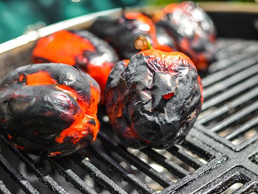 Red bell pepper being roasted on a grill; its skin charred and blackened. 