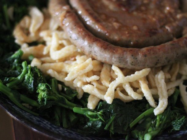 Spaetzle served in a bowl, alongside steamed broccoli and a coil of slender sausage.