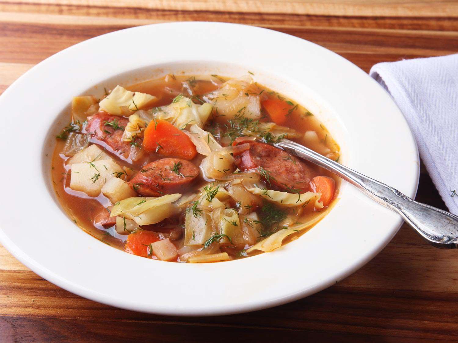 White bowl filled with sausage and cabbage soup on a wooden table