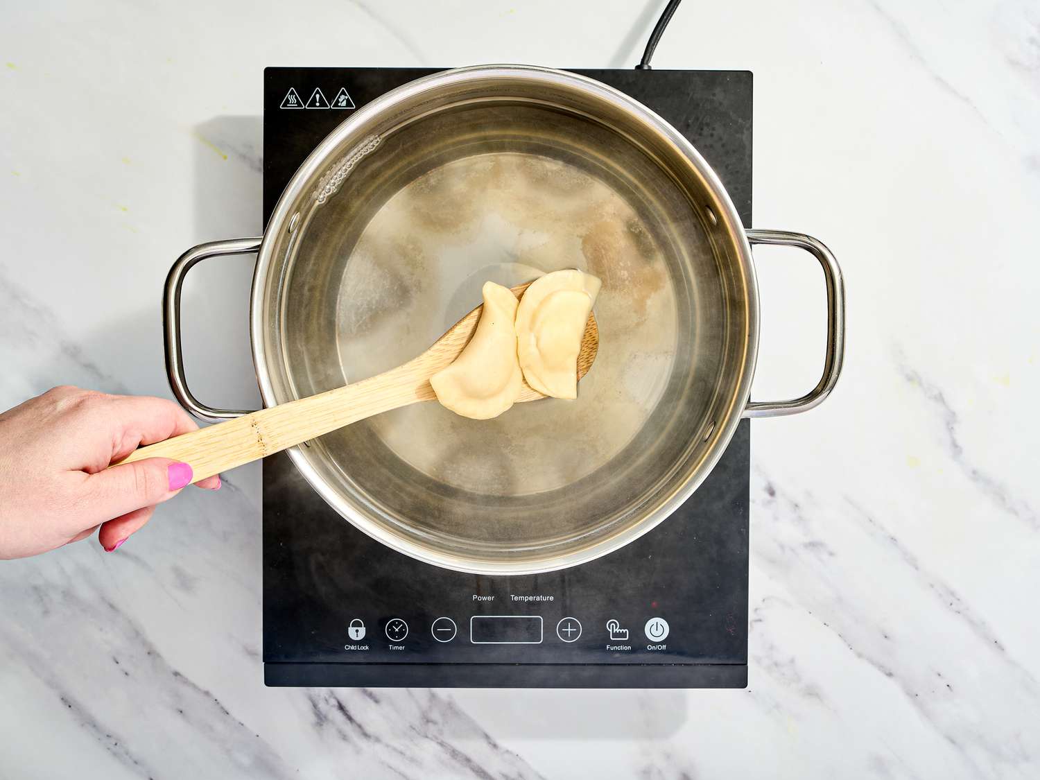 Placing dumplings into large pot of boiling water with a wooden spoon