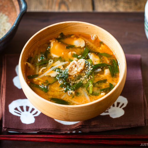 A light wooden bowl containing Spicy Pork and Bean Sprout Miso Soup sprinkled with ground sesame seeds.