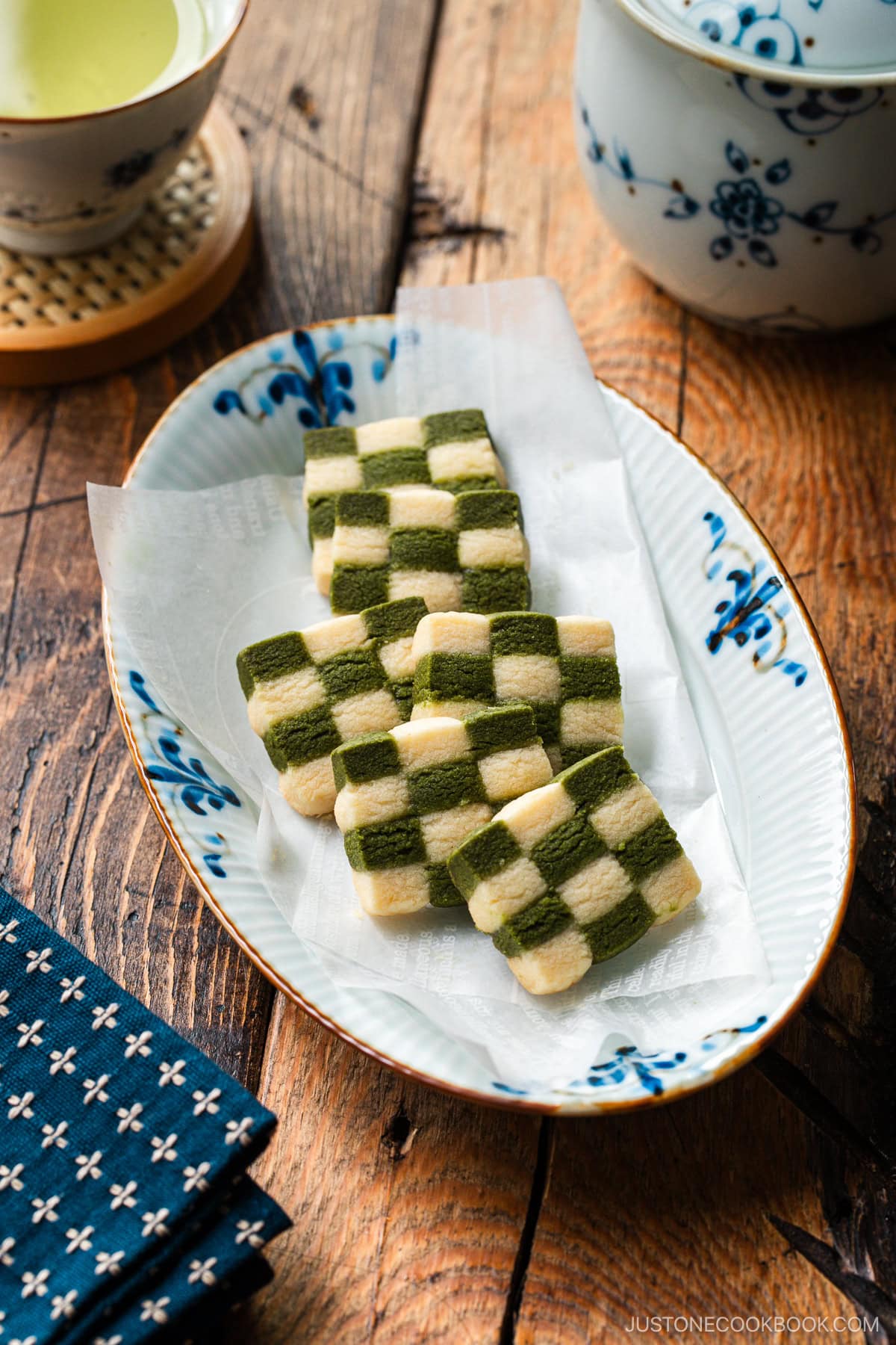 An oval plate containing Matcha Checkerboard Cookies served with a cup of green tea.