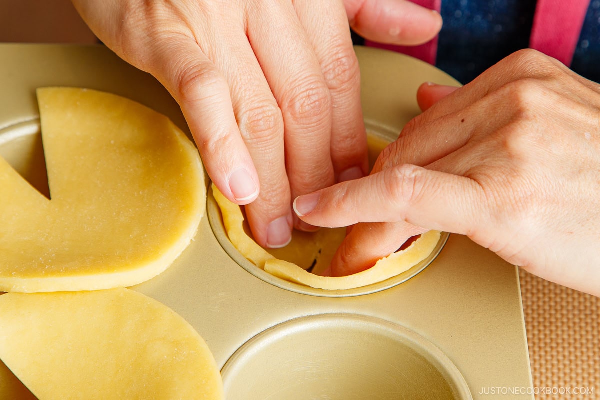 Gently pressing down the pastry into the cupcake pan.