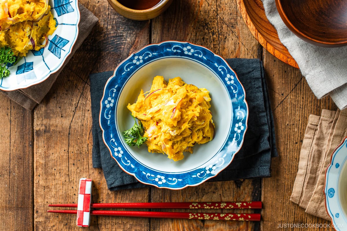 A Japanese round plate containing velvety and rich Kabocha Salad with crisp and refreshing red onion slices and ham, mixed with cream cheese and tangy Japanese mayo.