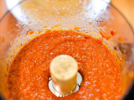 Roasted red pepper, eggplant, and garlic being ground in a food processor. 