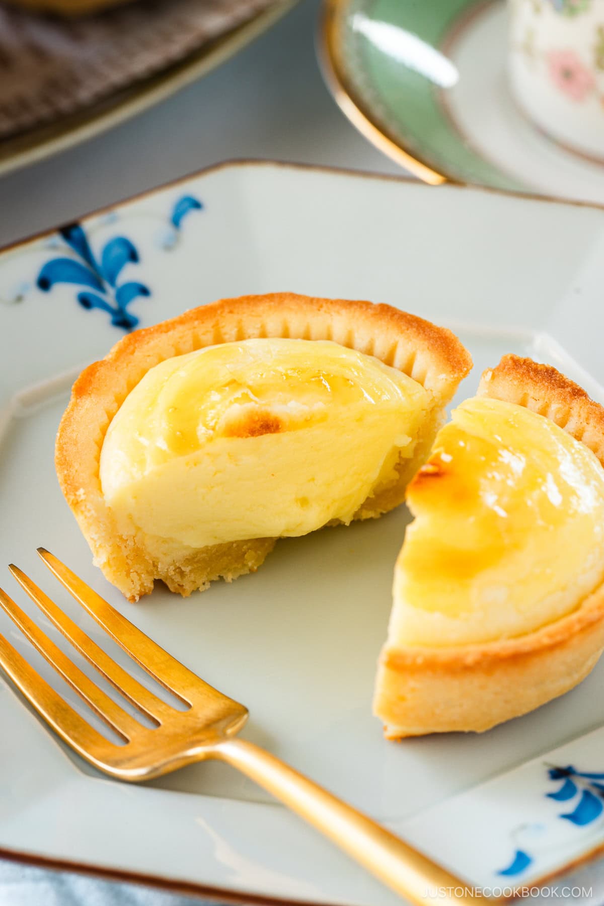 An octagon plate containing baked cheese tart, cut in half, creamy, soft cheese melting and oozing out from the crispy crust.