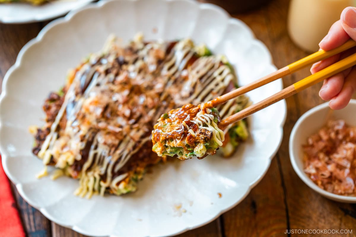 Chopsticks picking up a bite of negiyaki, a Japanese scallion pancake.