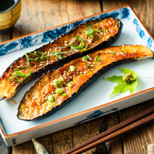 A rectangular plate containing Miso Glazed Eggplant garnished with yuzu kosho paste on a green maple leaf on the side.