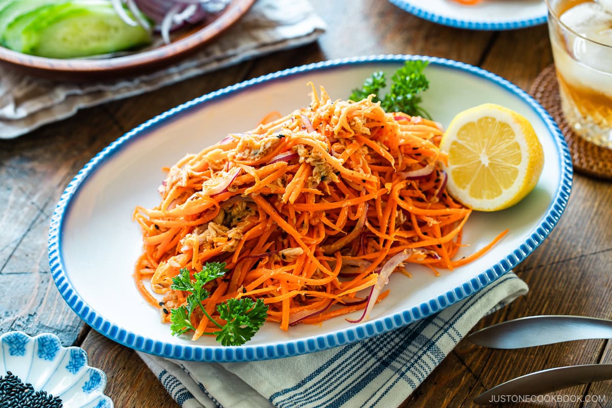 An oval scalloped plate containing shredded carrot and tuna salad garnished with parsley and lemon.