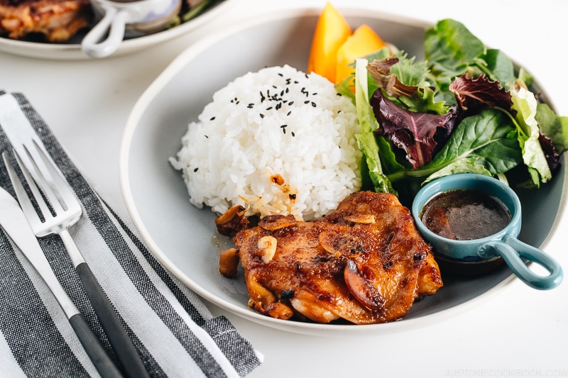 A large gray plate containing garlic onion chicken, green leaf salad, and steamed rice.