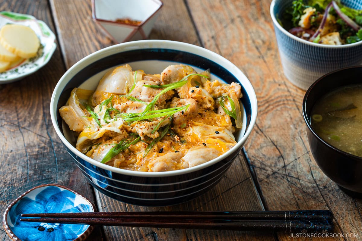 A Japanese ceramic bowl containing Oyakodon, a chicken and egg rice bowl dish garnish with green onion.
