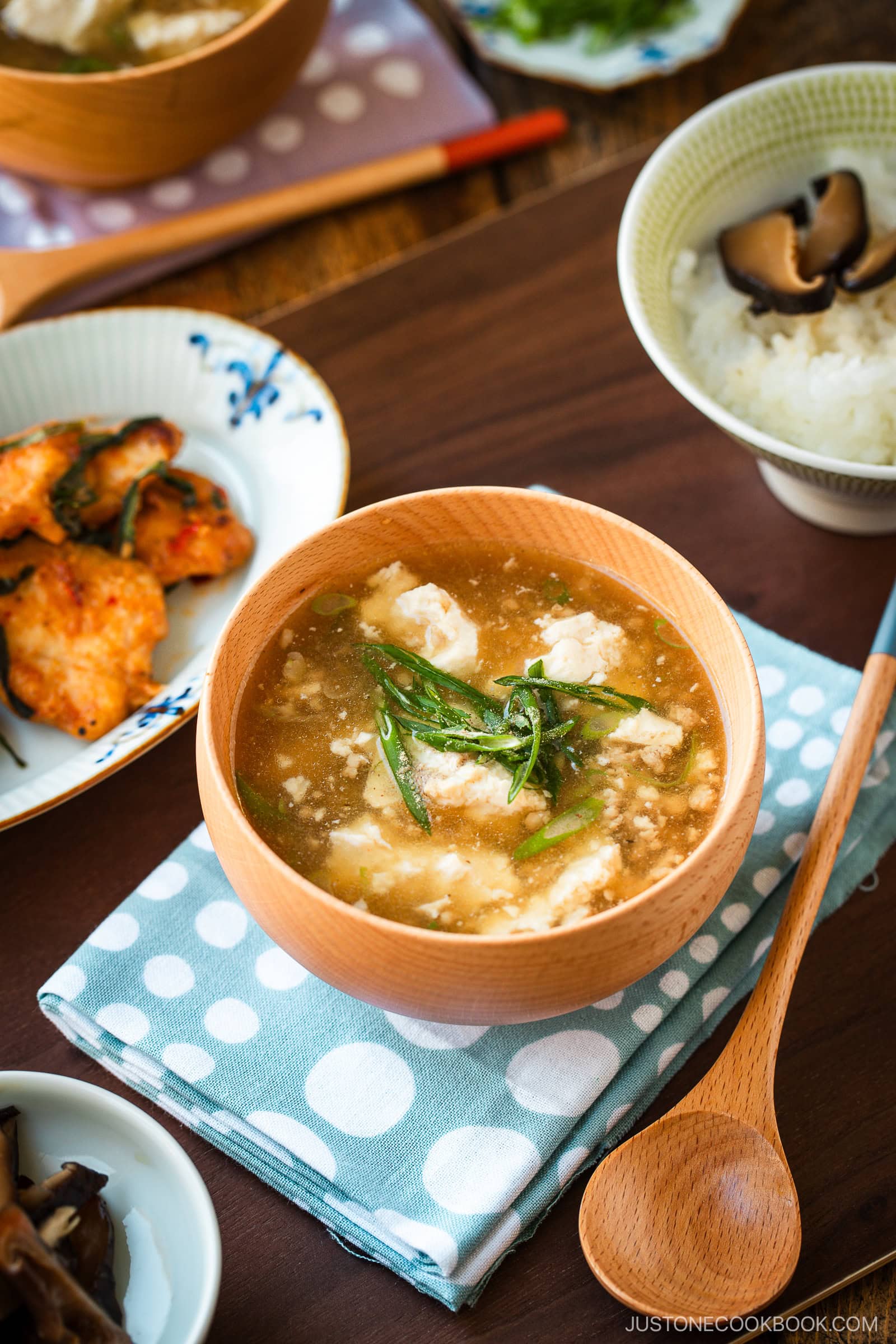 Wooden bowls filled with Pork Tofu Soup, served alongside steamed rice and a chicken dish on the table.