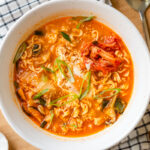 A white ramen bowl containing Korean ramen (ramyeon), topped with soft-cooked egg, kimchi, and green onions.